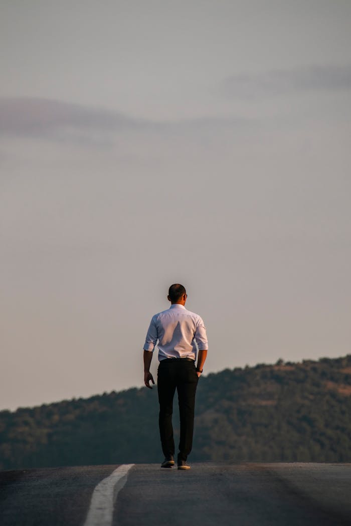 A man walks alone down an empty mountain road, symbolizing solitude and introspection.